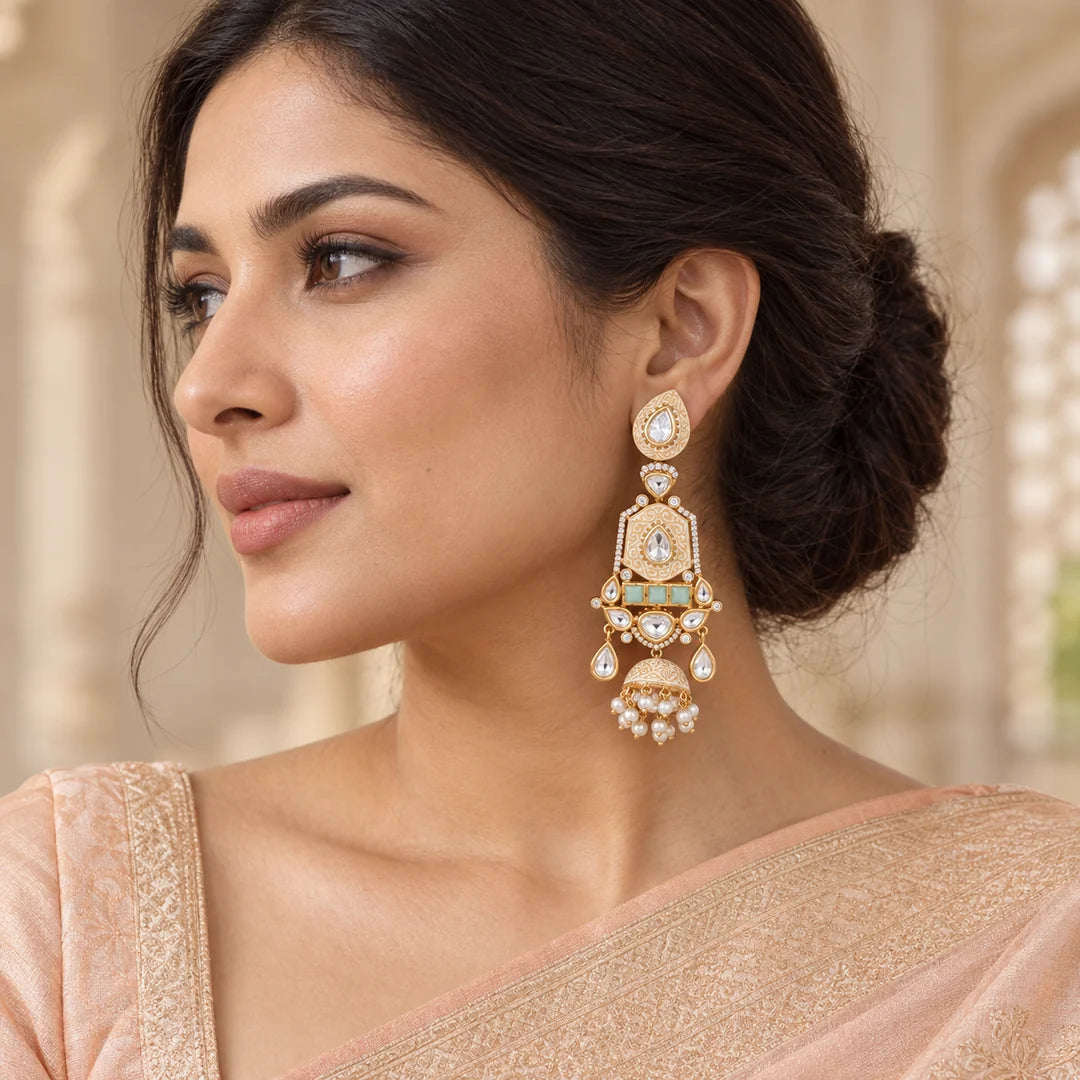 Pair of ivory and mint long jhumka earrings with gold-tone scrollwork, clear stones and pearl-look fringe on a black background.
