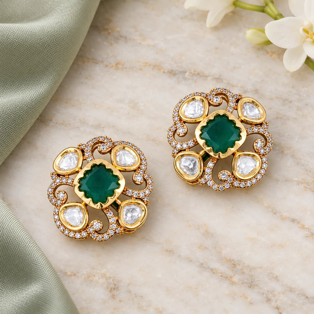 Pair of Ishani  green floral stud earrings with clear stones and gold-tone openwork on ivory stone beside sage silk.