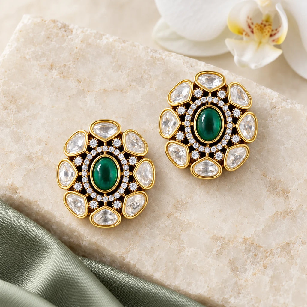 Pair of Ishani green Kundan-style floral stud earrings on ivory stone beside sage silk and a white orchid.