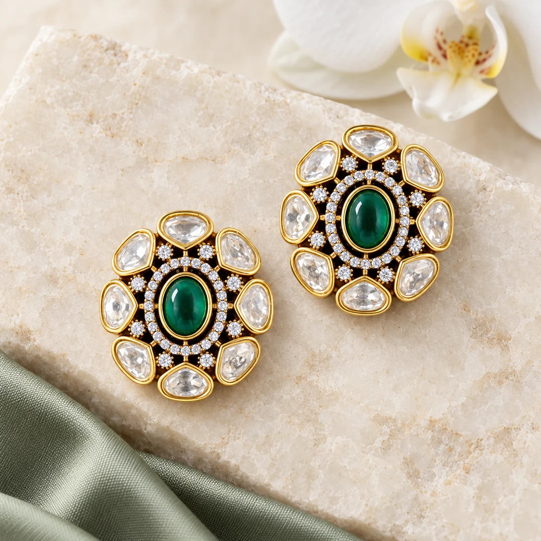 Pair of Ishani green Kundan-style floral stud earrings on ivory stone beside sage silk and a white orchid.