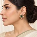 Side-profile Indian model wearing an Ishani green oval stud earring surrounded by clear stones in gold-tone settings.