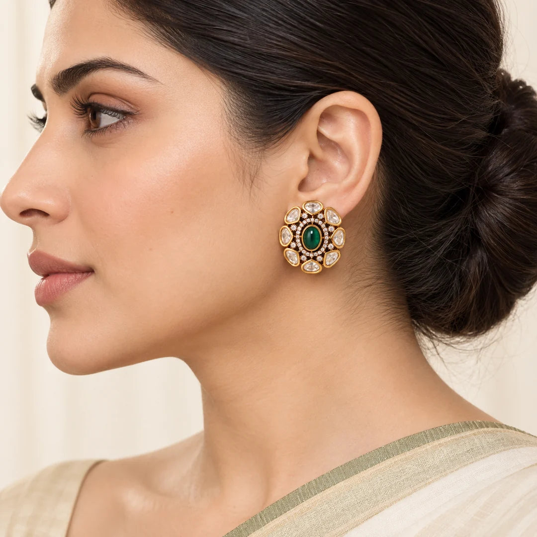 Side-profile Indian model wearing an Ishani green oval stud earring surrounded by clear stones in gold-tone settings.