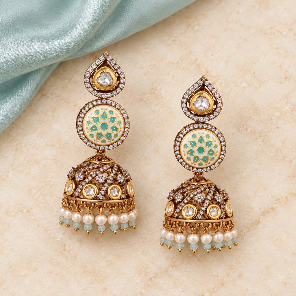 Pair of Kalika ivory and mint floral jhumka earrings on cream stone beside pale aqua silk, showing detailed gold-tone domes.