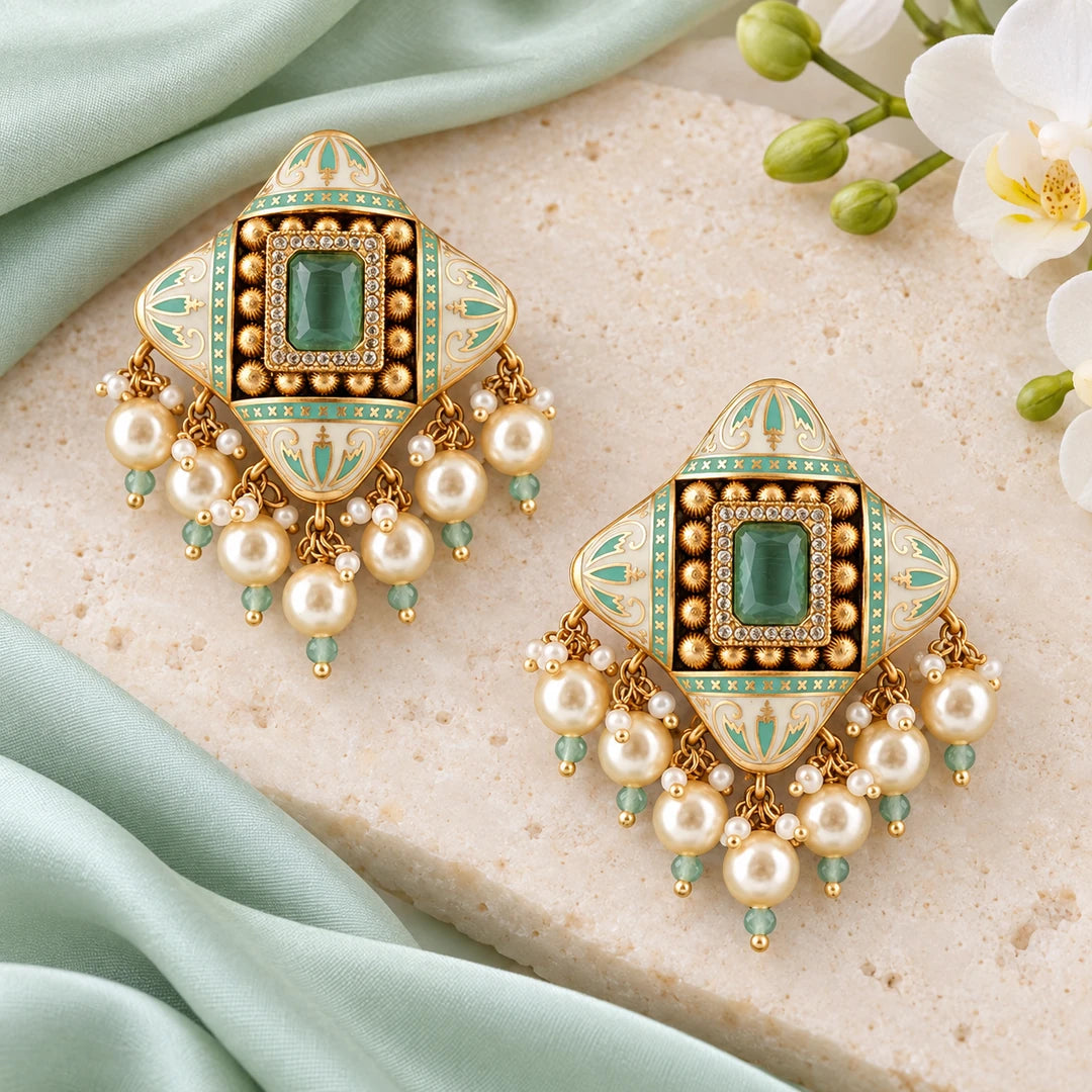Pair of Kalindi ivory and mint pearl-style earrings on cream stone beside pale mint silk and a white orchid.