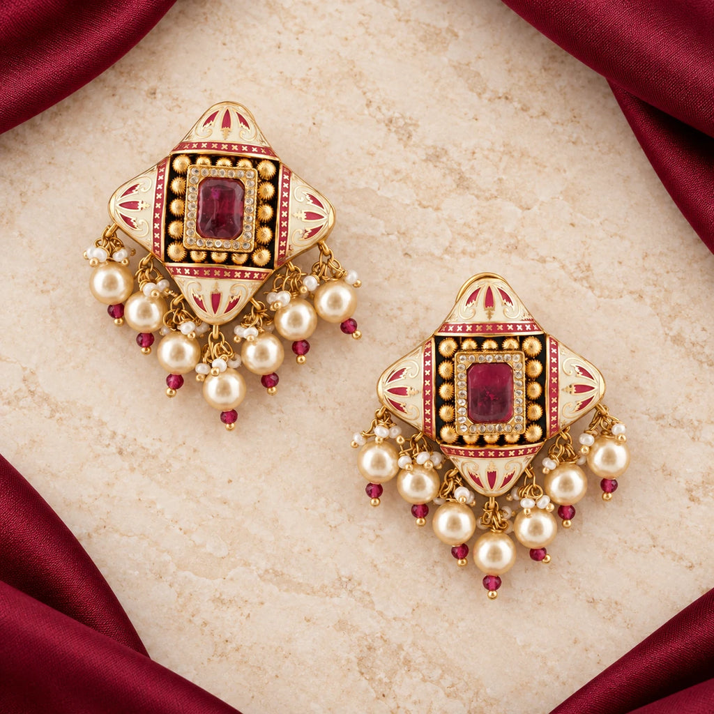Pair of Kalindi ivory and ruby-colour pearl-style earrings on cream stone framed by burgundy fabric.