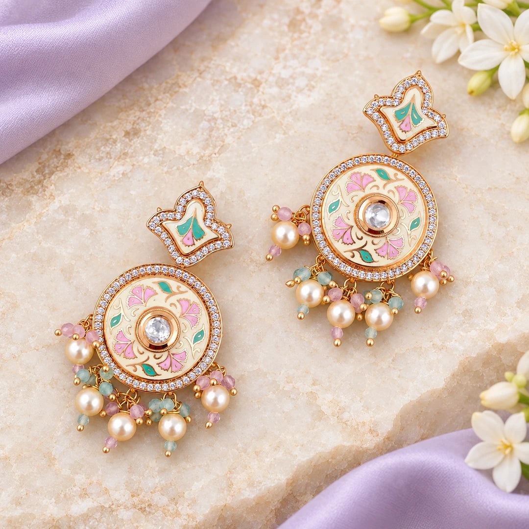 Pair of Kalpita ivory and pastel floral drop earrings on cream stone beside lavender silk and white flowers.