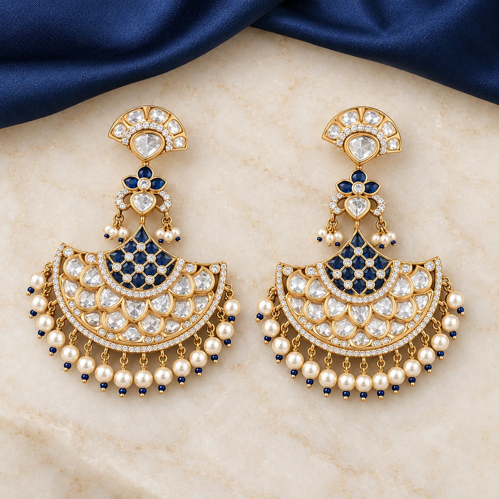 Pair of Kalyani navy-blue and pearl-style chandbali earrings on ivory stone beside navy fabric, showing lattice-style centres and clear teardrop stones.