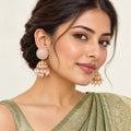 Model in a sage-green silk saree wearing Kamala ivory and blush jhumka earrings with clear stones and cream pearl-style fringe.