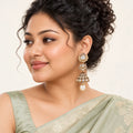 Indian model with a curly updo wearing a sage saree and Kamya clear jhumka earrings with cream pearl-style drops.