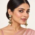 Indian model in a blush saree wearing Kamya green jhumka earrings with tiered gold-tone domes and cream pearl-style drops.