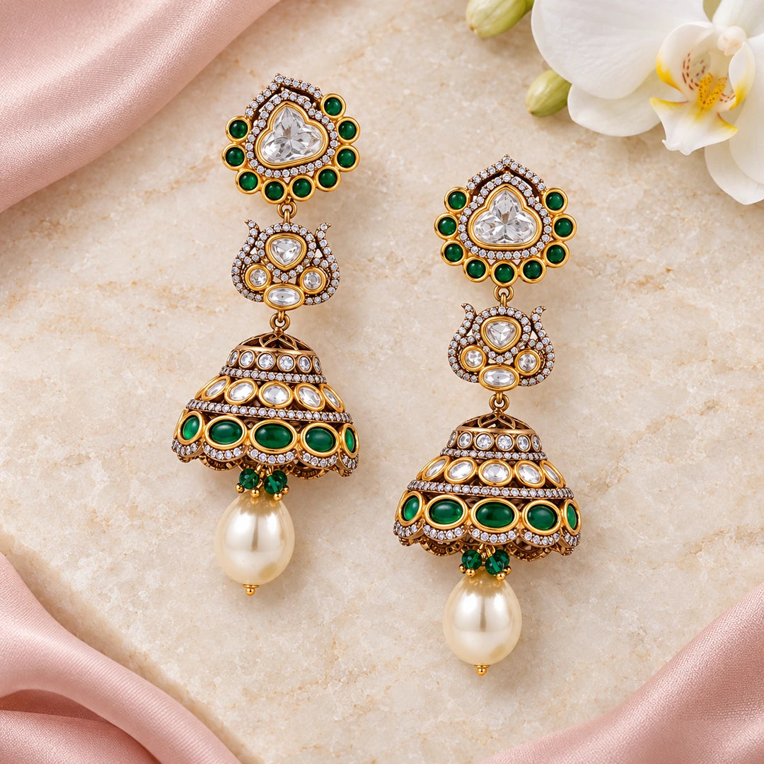 Pair of Kamya green and pearl-style jhumka earrings on cream stone beside blush silk and a white orchid.