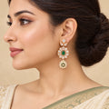 Model wearing a Kamya ivory and green floral drop earring with an ivory saree and sage border, hair swept into a bun.