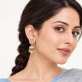 Indian model in a powder blue saree wearing a Kanavi ivory and turquoise jhumka earring with clear floral detailing and pearl-style drops.