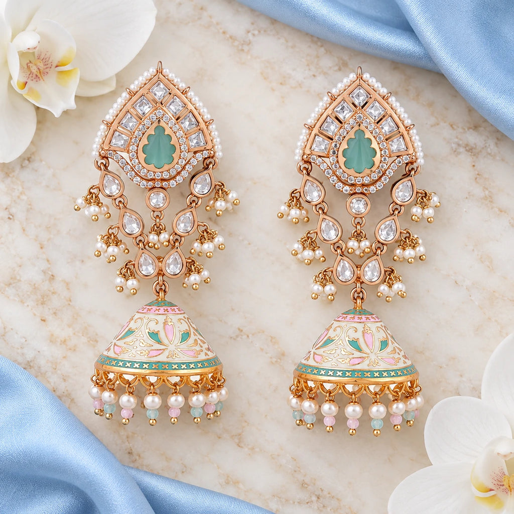 Pair of Kanishka ivory and pastel long jhumka earrings on cream stone beside powder blue silk and white orchids.