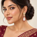 Model wearing a Kashmira floral teardrop earring with ruby-colour bead edging, styled with burgundy traditional clothing.

