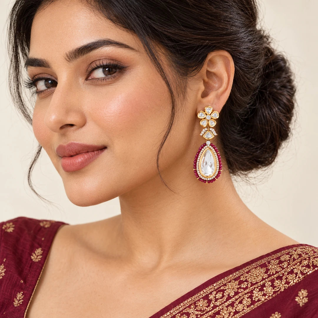 Model wearing a Kashmira floral teardrop earring with ruby-colour bead edging, styled with burgundy traditional clothing.


