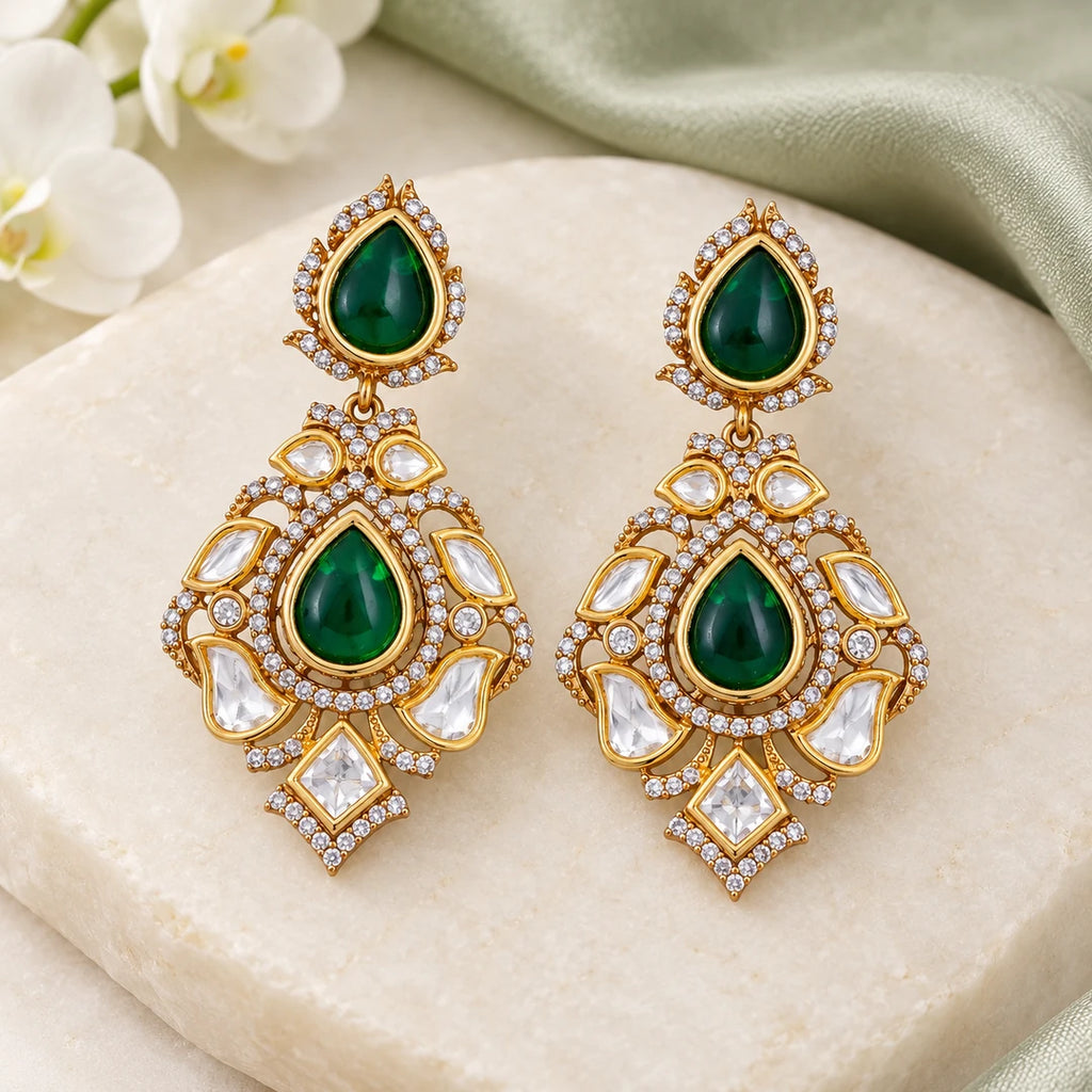 Pair of Kashvi green teardrop earrings with clear stones displayed on a gold-tone stand against a pale background.