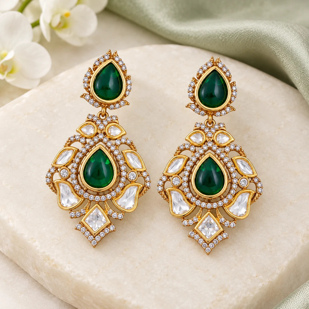 Pair of Kashvi green teardrop earrings with clear stones displayed on a gold-tone stand against a pale background.