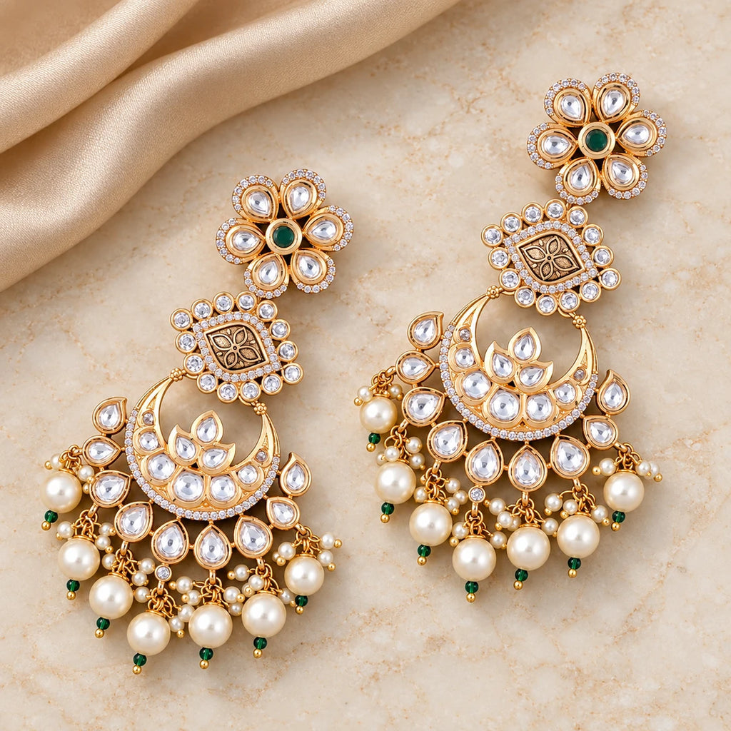 Pair of Kaumudi chandbali earrings with green floral centres, engraved gold-tone connectors and cream pearl-style drops on cream stone beside champagne silk.
