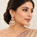 Indian model wearing Kaumudi ruby-colour chandbali earrings with cream pearl-style drops and a champagne saree with a mauve border.