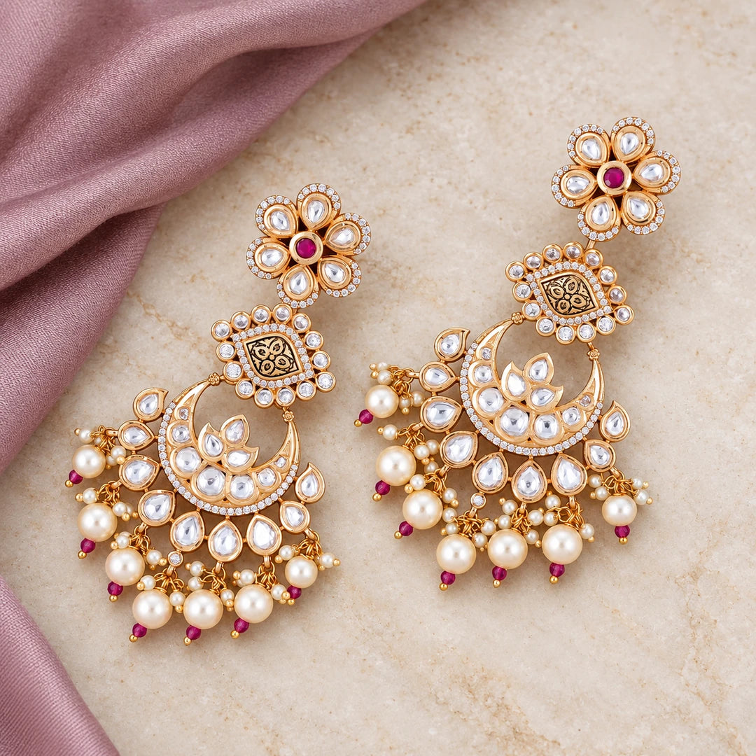 Pair of Kaumudi ruby-colour chandbali earrings with floral tops and cream pearl-style drops on cream stone beside dusty mauve silk.