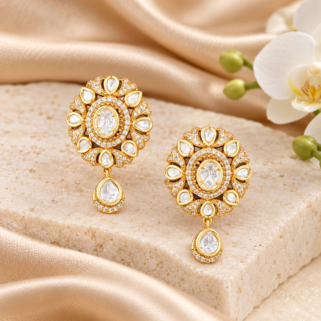Pair of Kaushiki gold-tone floral drop earrings with oval clear centres, pear-shaped accents and teardrop pendants on a dark background.