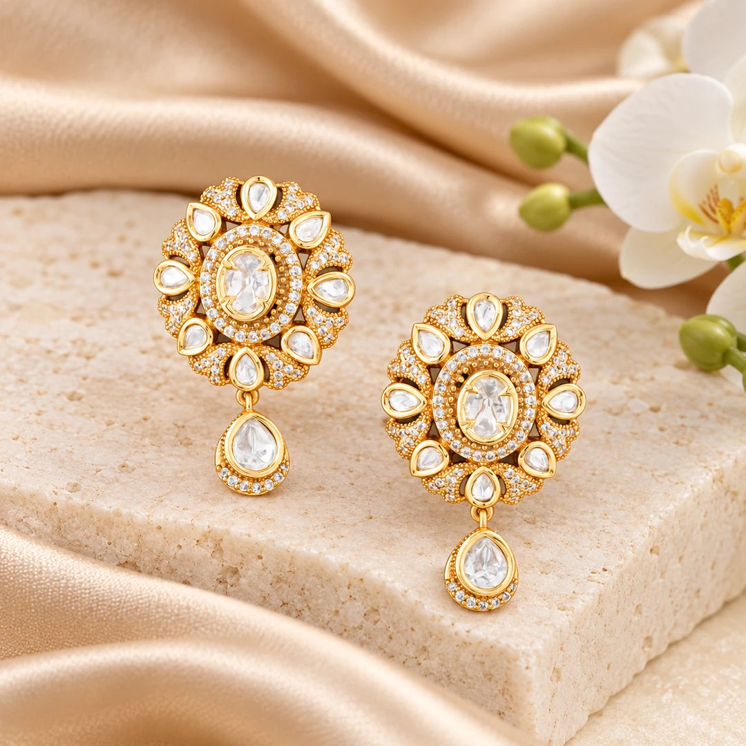 Pair of Kaushiki gold-tone floral drop earrings with oval clear centres, pear-shaped accents and teardrop pendants on a dark background.