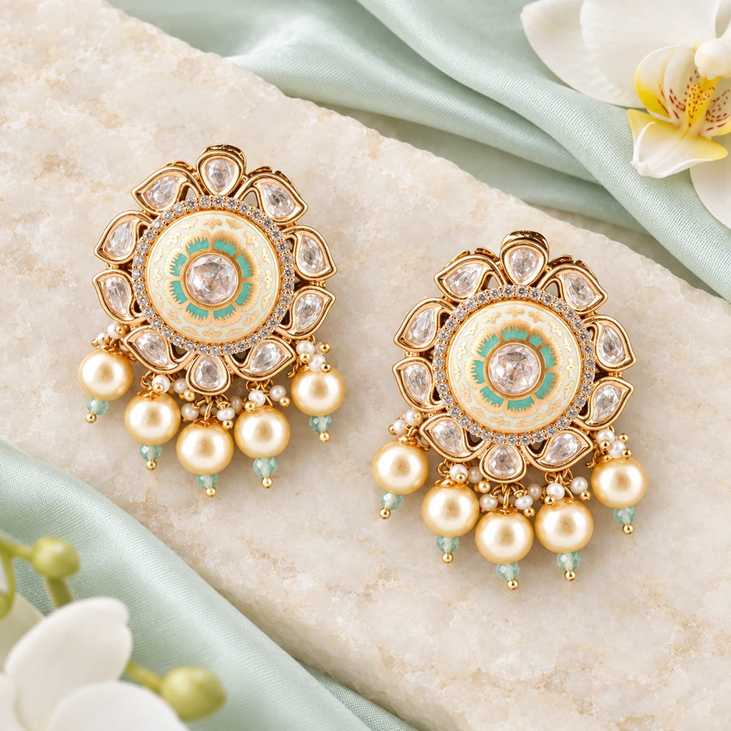 Pair of Kavini ivory and mint pearl-style earrings on cream stone beside pale mint silk and white orchids.