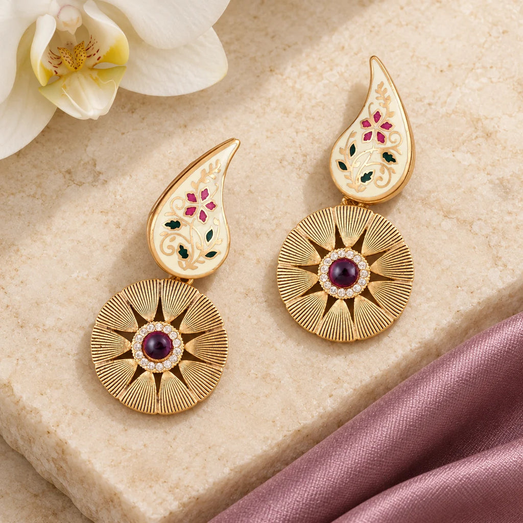 Pair of Kavya ivory and ruby-colour floral drop earrings on cream stone beside mauve silk and a white orchid.