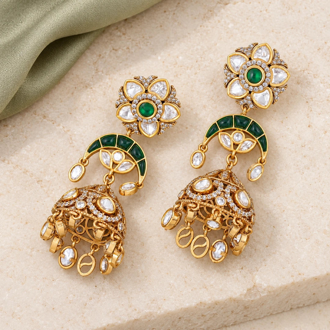 Pair of Keshavi green floral jhumka earrings with gold-tone domes and oval clear stone drops on cream stone beside sage fabric.