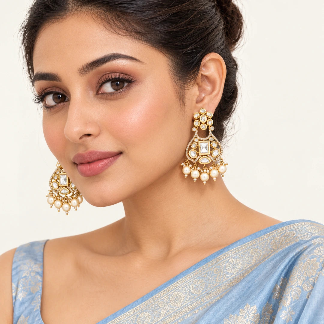 Model in a powder-blue silk saree wearing Ketaki clear chandelier earrings with gold-tone detailing and cream pearl-style drops.