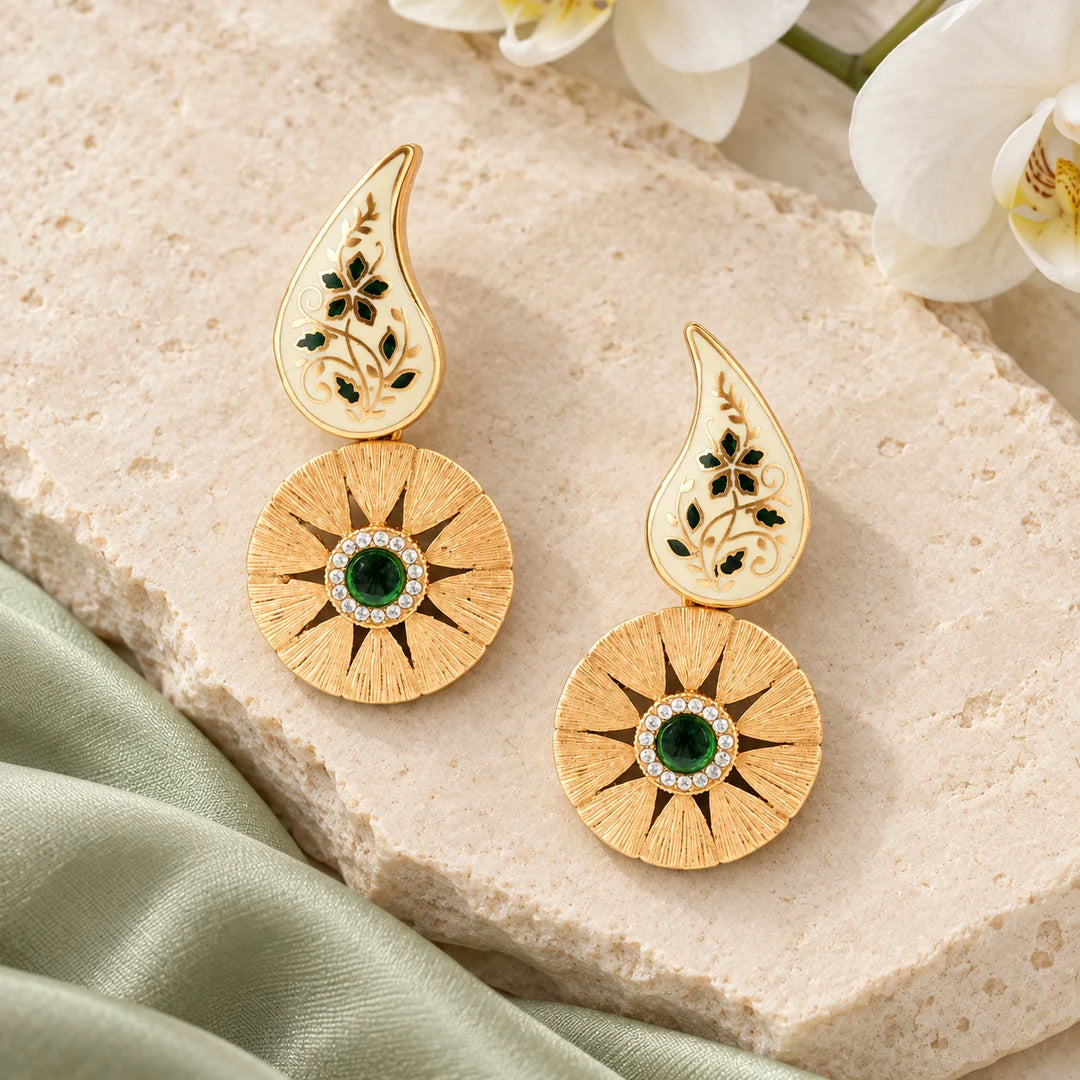 Pair of Ketaki ivory and green floral drop earrings on cream stone beside sage silk and a white orchid.