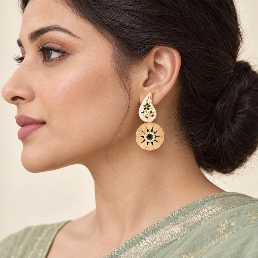 Model in side profile wearing a Ketaki ivory paisley earring with green floral details and a textured gold-tone circular drop.