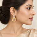 Model in side profile wearing a Kiran ivory paisley earring with ruby-colour floral details and a textured gold-tone circular drop.