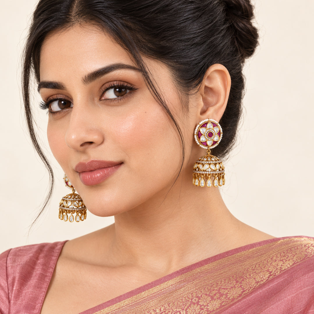 Indian model in a dusty rose saree wearing Kiranya ruby-colour floral jhumka earrings with gold-tone domes and clear teardrop fringe.