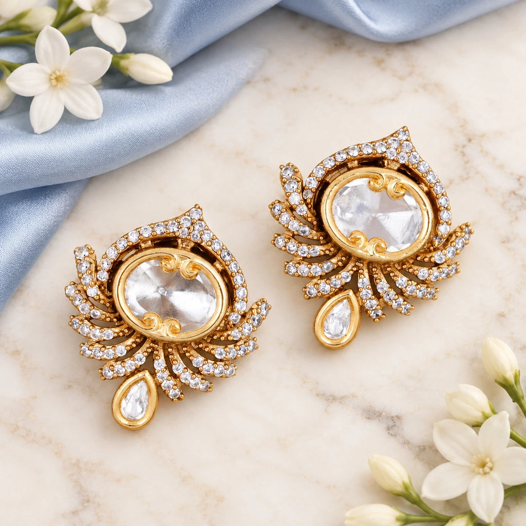 Pair of Koshika clear fan-style earrings on cream stone beside powder blue silk and white jasmine flowers.