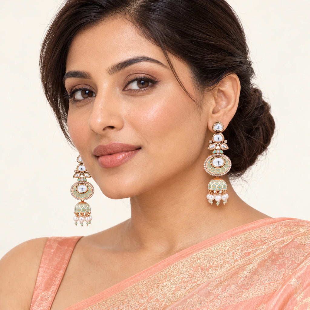 Model wearing a peach saree and Kritara ivory and mint jhumka earrings with clear stones and cream pearl-style drops.