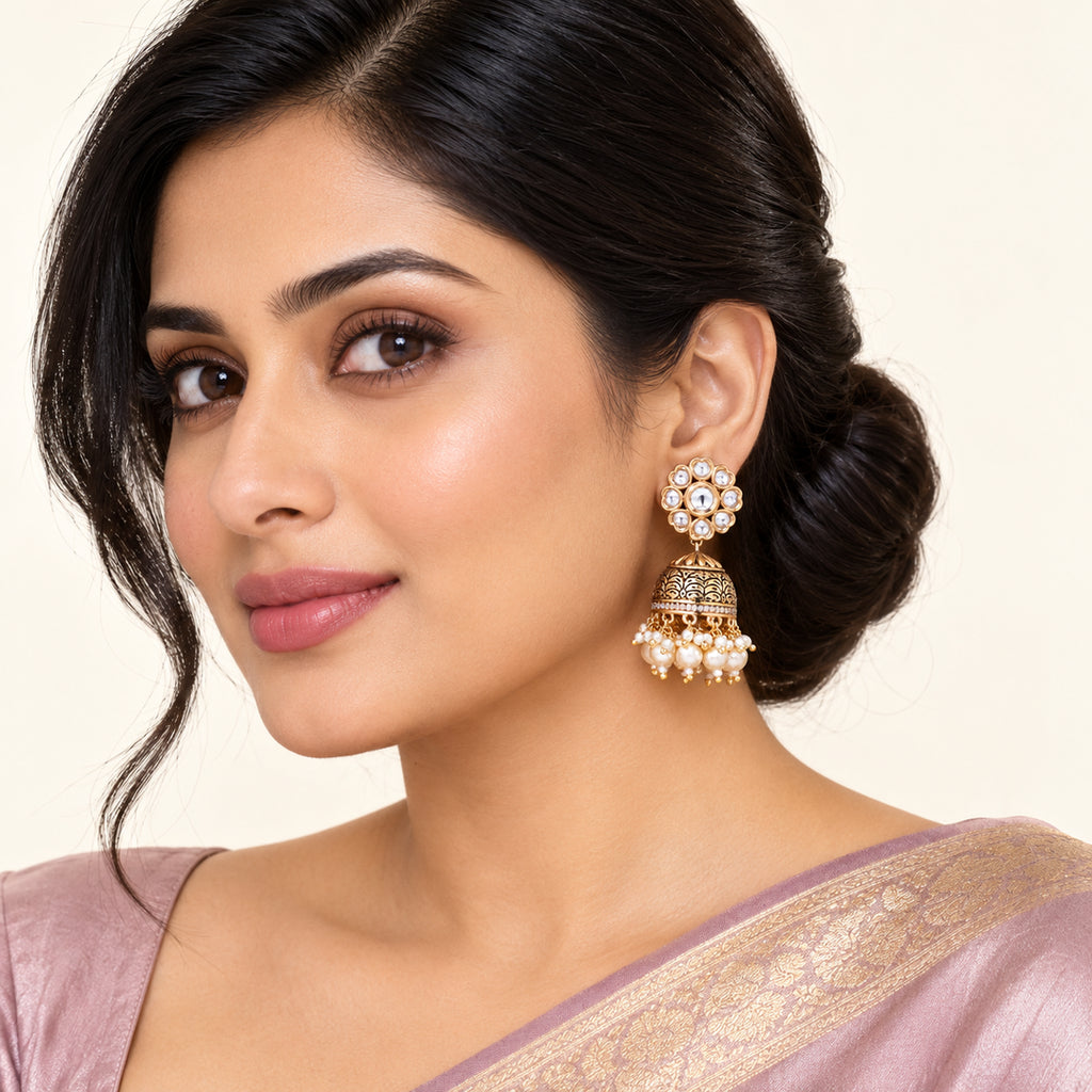 Model wearing Kritika clear floral and cream pearl-style jhumka earrings with a pale mauve saree against a cream studio background.