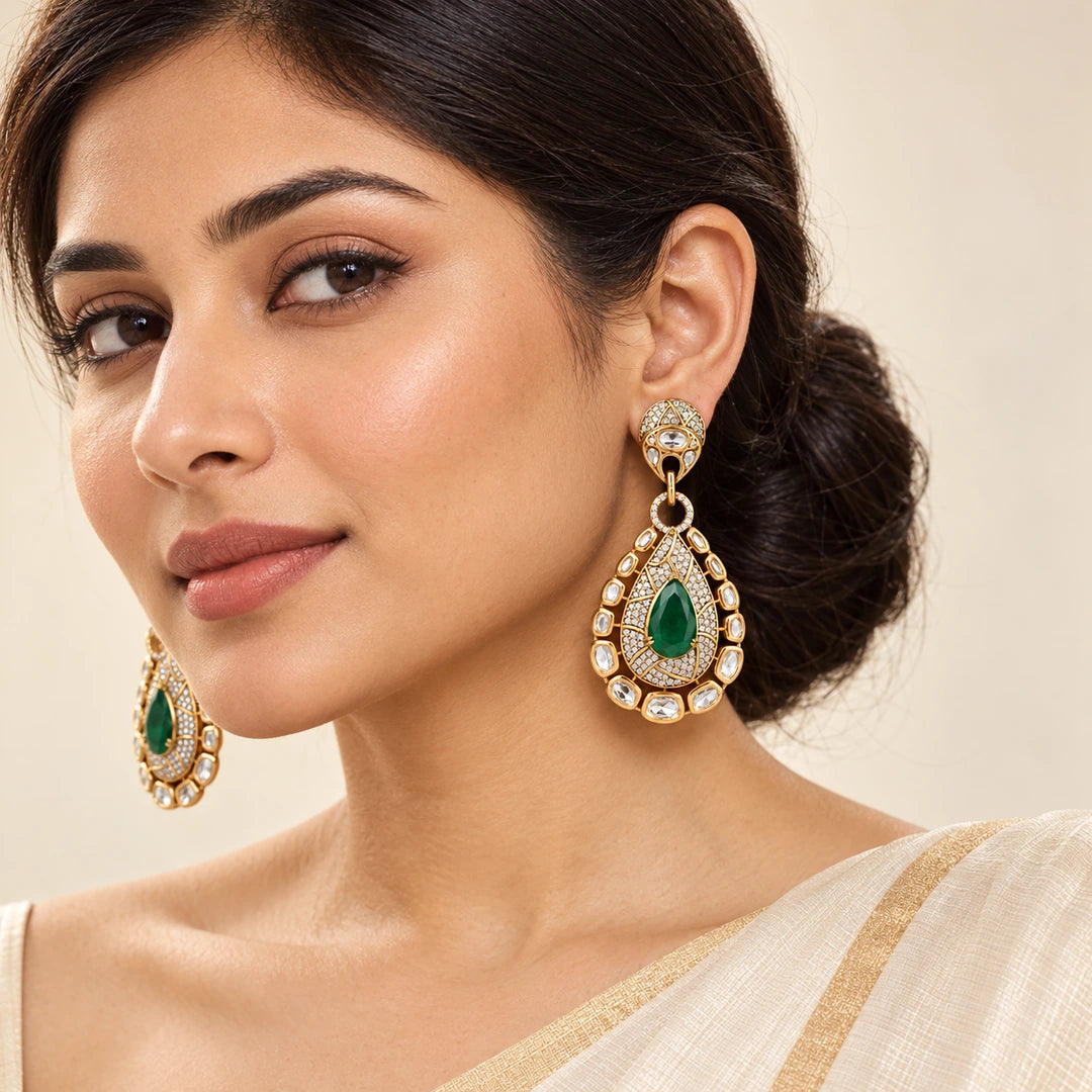 Indian model in an ivory saree wearing Kritvi green teardrop earrings with clear-stone borders and gold-tone detailing.