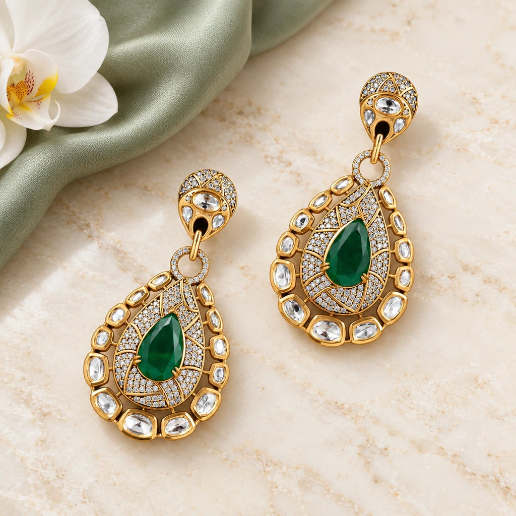 Pair of Kritvi green teardrop statement earrings on cream stone beside sage silk and a white orchid.