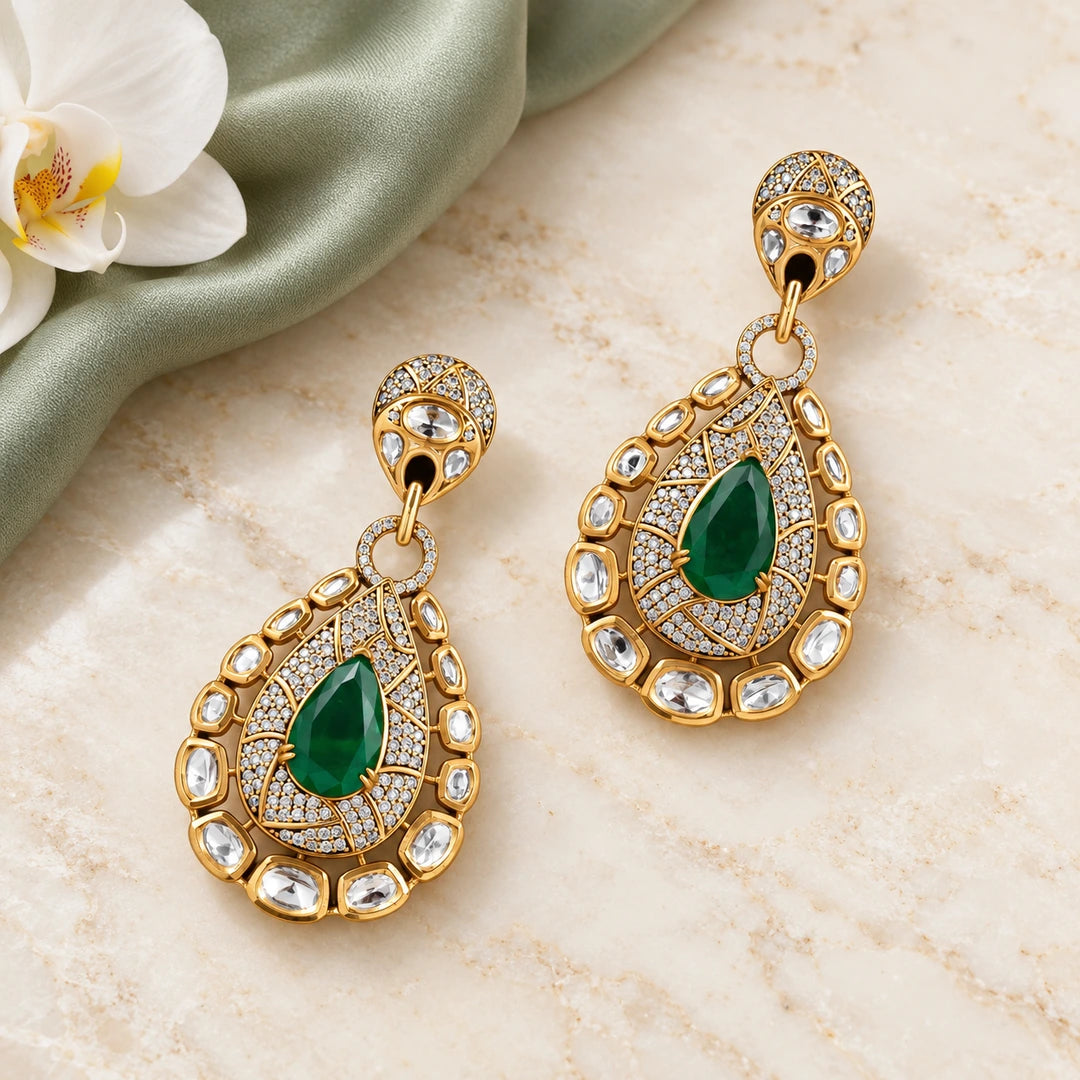 Pair of Kritvi green teardrop statement earrings on cream stone beside sage silk and a white orchid.