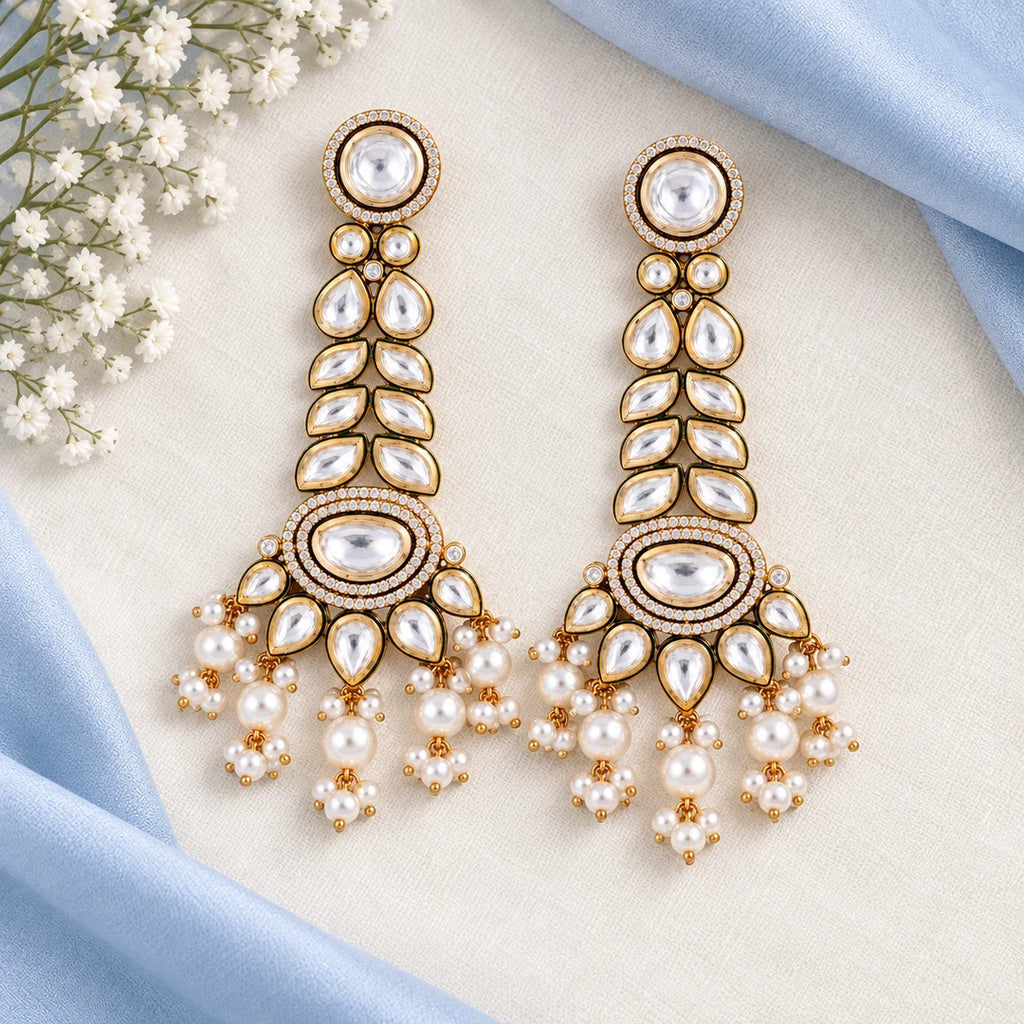 Pair of clear-stone leaf-pattern earrings with white pearl-look tassels on an ivory display against pale blue silk.