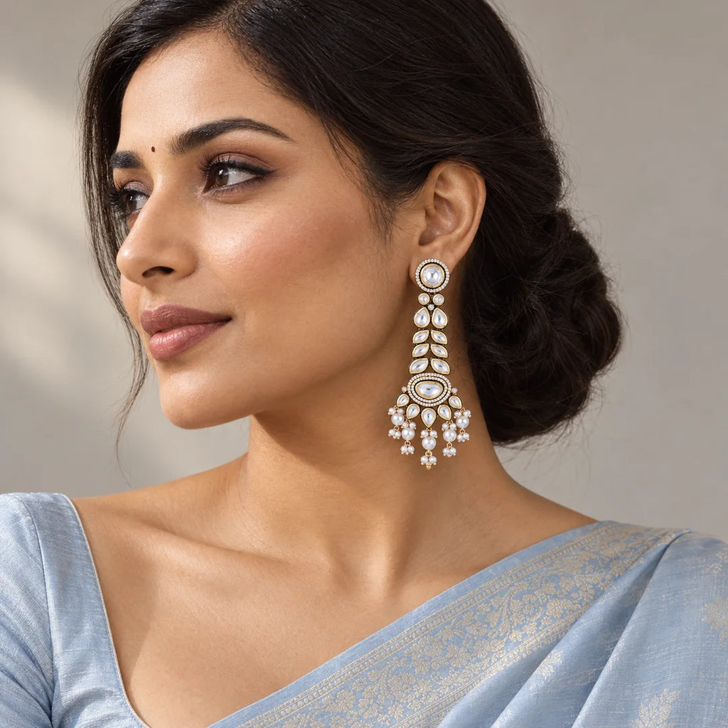 Indian model in a powder blue saree wearing a long gold-tone earring with clear leaf-shaped stones and white pearl-look tassels.