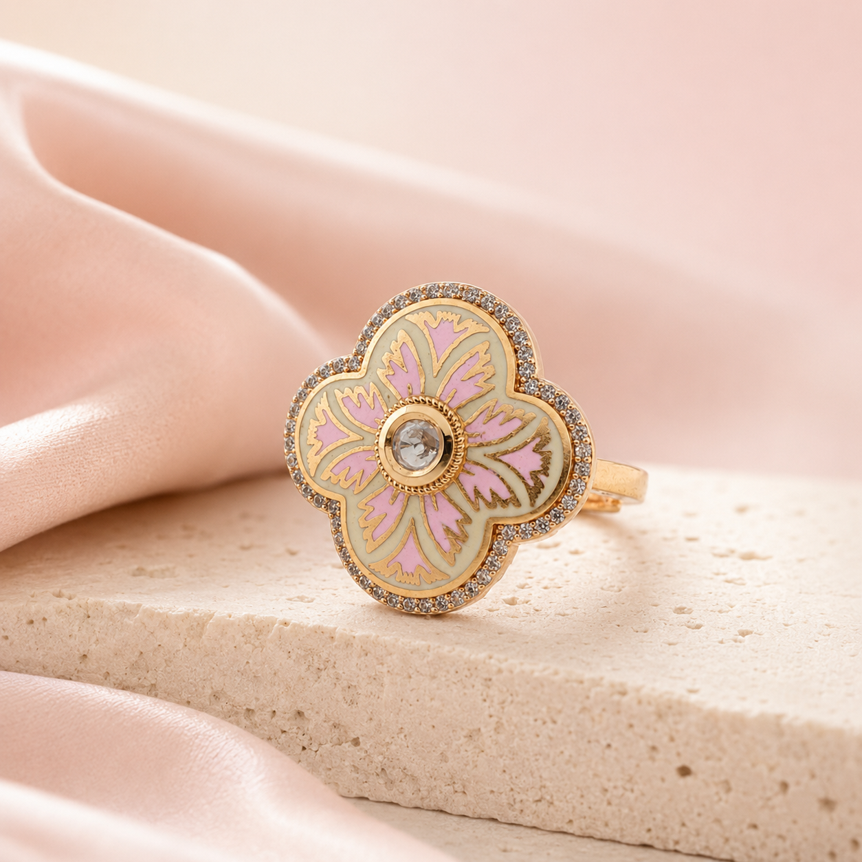 Gold-finish pink floral cocktail ring displayed on a neutral stone surface