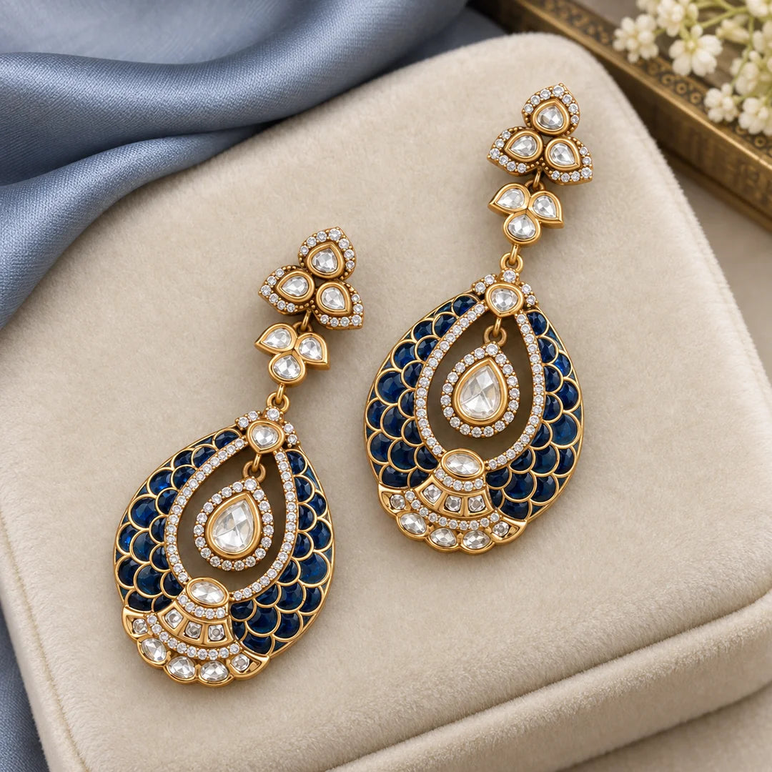 Pair of Mayura blue teardrop earrings with scalloped detailing on an ivory velvet display beside blue silk.