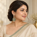 Indian model in an ivory saree with a sage border wearing a Mayura green teardrop earring with clear stones.