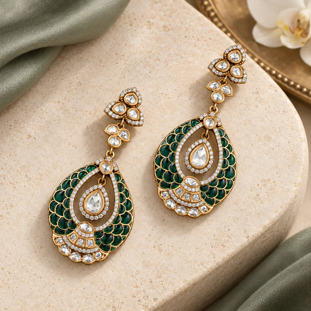 Pair of Mayura green teardrop earrings on a cream stone display with sage silk and a white orchid.