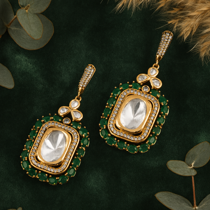 Gold and green earrings on a dark green background with leaves.
