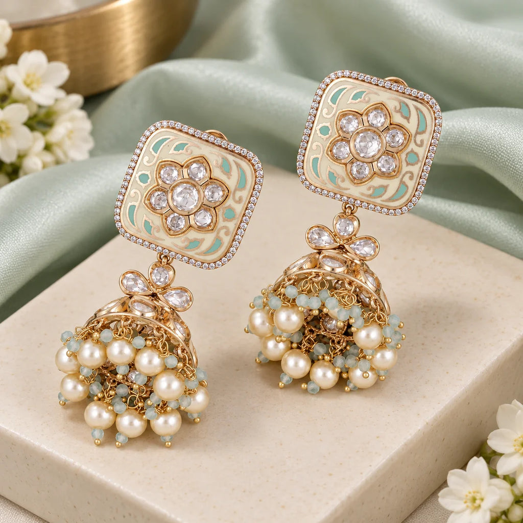 Pair of ivory and mint floral jhumka earrings styled on a cream display beside mint fabric and white flowers.