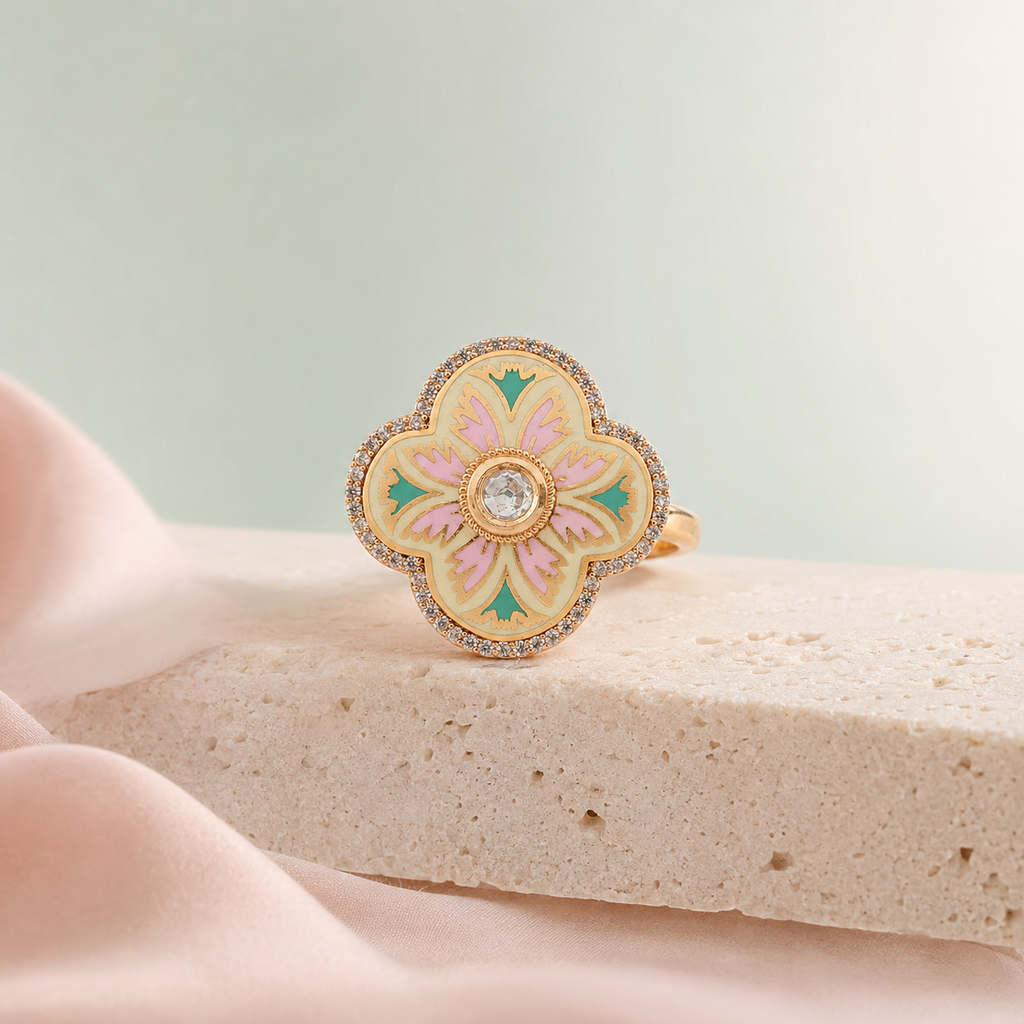 Gold-finish floral ring with pastel detailing displayed on a stone surface